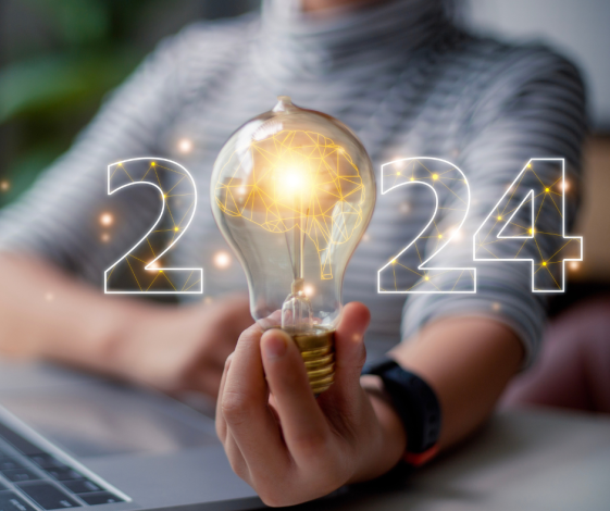 パソコンの前で電球を手にする女性、2024の文字が電球に重なるイメージ画像